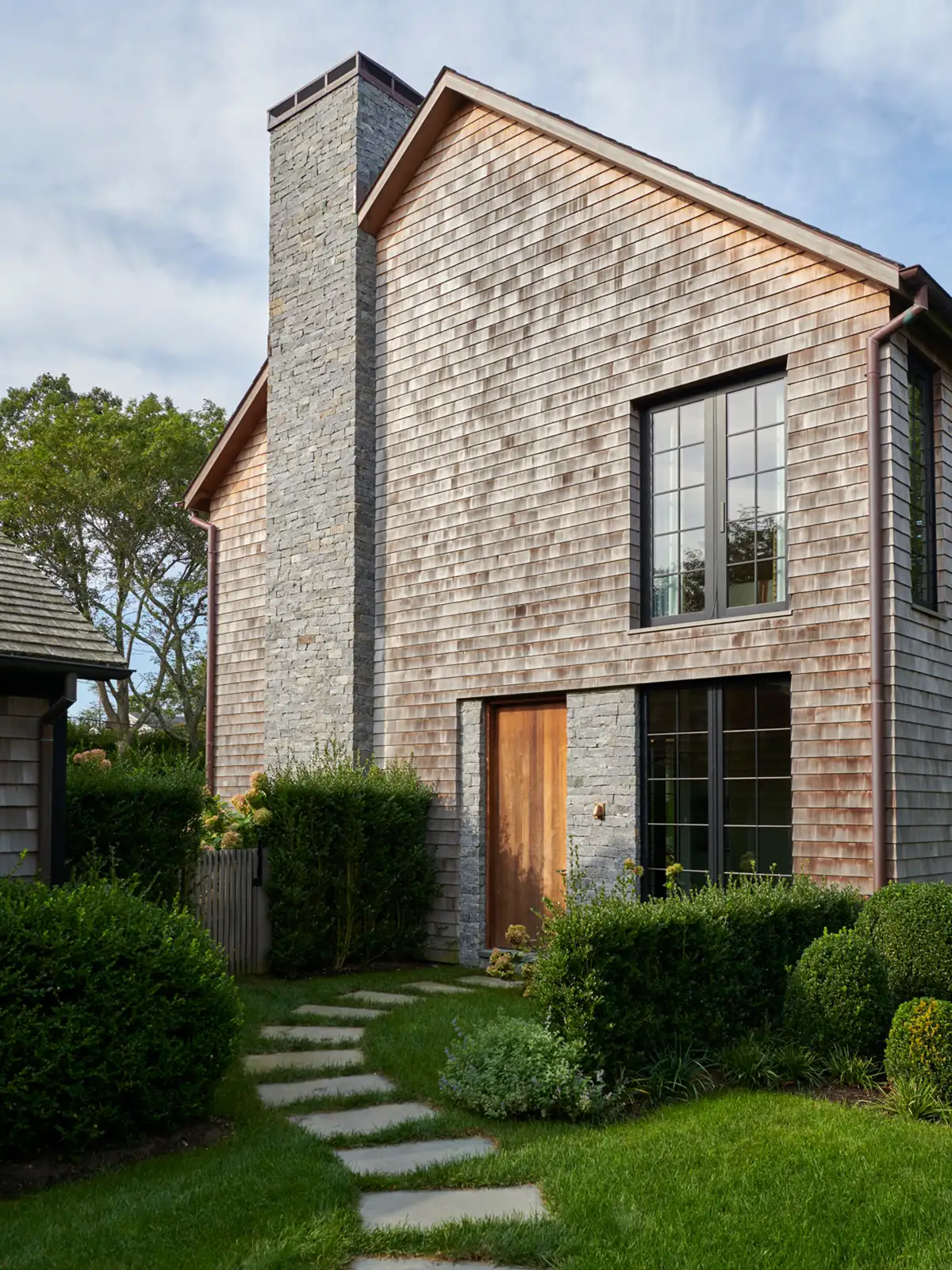 The exterior of the newly constructed single home family has a gray palette with warm and cool tones due to the ash rainscreen siding; the stone and slate gable style roof, respectively.  
