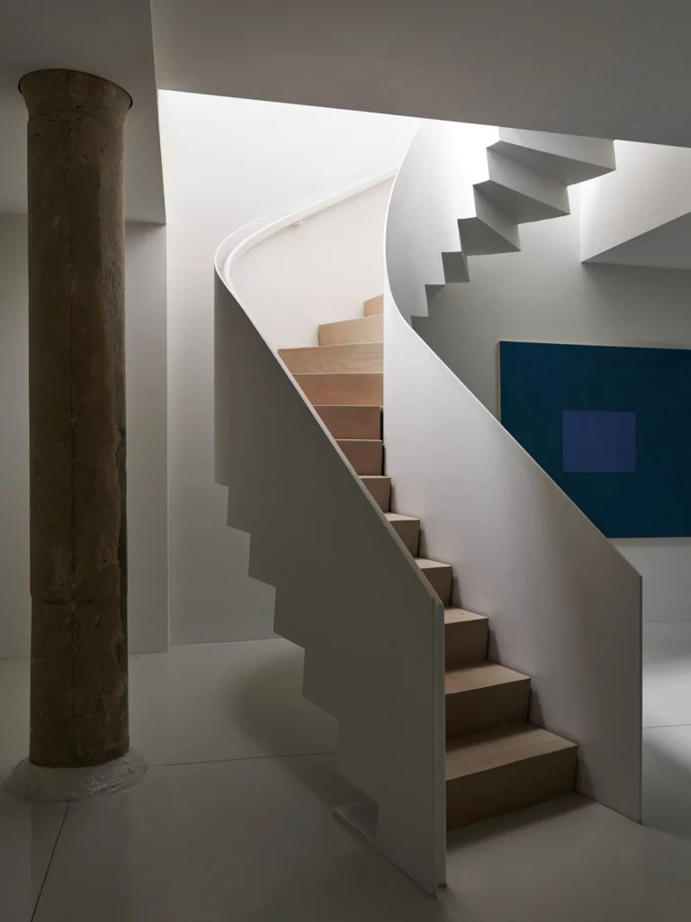 Sculptural steel stair illuminated by a skylight above.