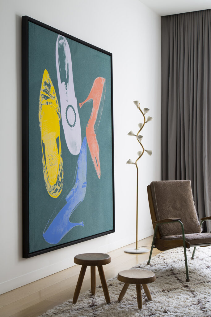 Corner of the living room featuring a Painting by Andy Warhol next to a n armchair by Jean Prouvé, a lamp by Gino Sarfatti, and tabourets by Charlotte Perriand.