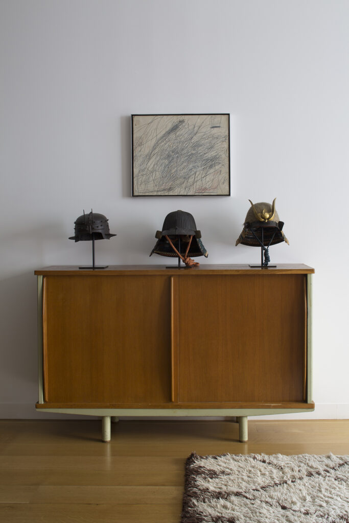 Cy Twombly painting hangs above Jean Prouvé cabinet on which sit a group of Japanese helmets.